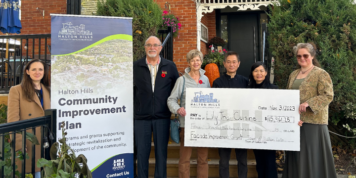 six people standing with a cheque in front of a brick building