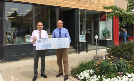 two men standing outside storefront with large cheque