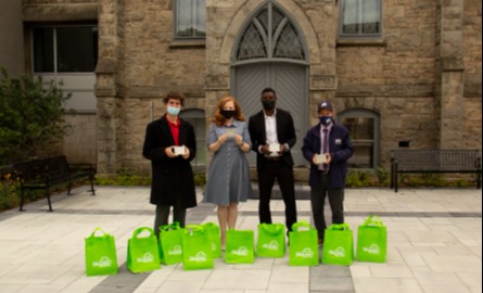 Four people standing outside with green bags
