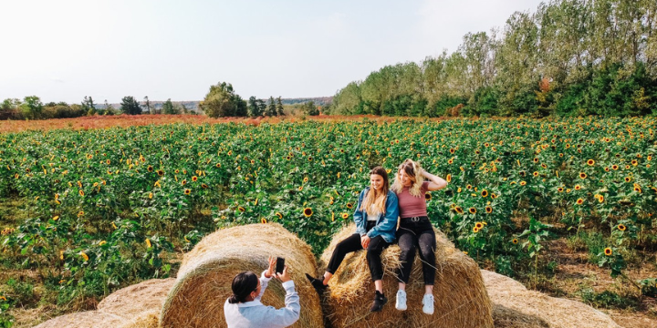 Person taking photo of two women on hay bale