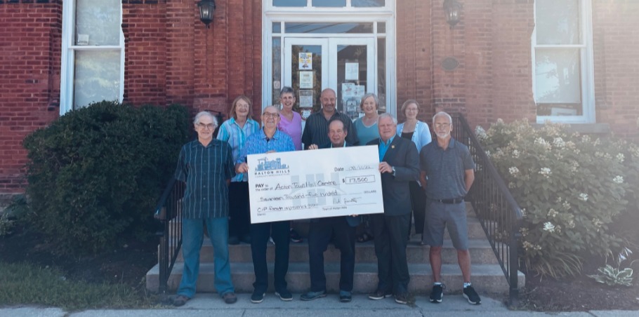 Group of people standing in front of a brick building holding a big cheque