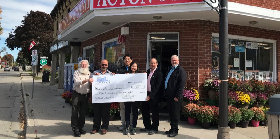 Group of people standing in front of a storefront holding a big cheque